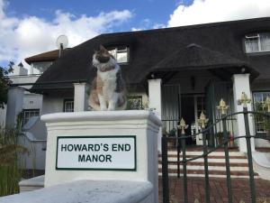 开普敦Howards End Manor B&B的坐在房子前面标志上的猫