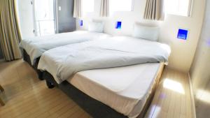 那霸Across Omoromachi Naha的配有白色床单的酒店客房内的两张床