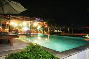 蓝梦岛Pemedal Beach Resort的夜间游泳池,配有桌子和遮阳伞