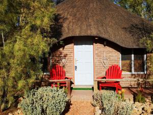 库斯Terra Rouge Guestfarm & Sonstraal Farmhouse的两把红色椅子坐在一座茅草屋顶的建筑前面