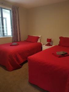 特威泽尔Rosedale Cottages的宿舍间的两张床,配有红色床单和窗户