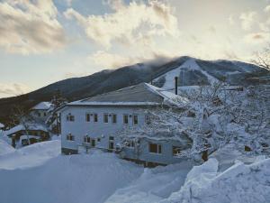 饭山市Raicho Lodge Madarao的一座雪覆盖的房子,背景是一座山