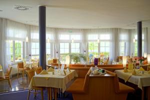 OlbersdorfHotel Haus am See的餐厅设有白色的桌椅和窗户。