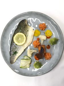 默兹河畔凡尔登Les Orchidées , Hôtel & Restaurant的一只盘子,上面有一条鱼,上面有柠檬和蔬菜