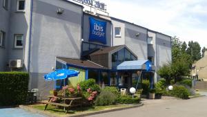 格朗德桑特Ibis budget Dunkerque Grande Synthe的蓝色的建筑,前面设有桌子和遮阳伞