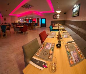 拉克塔希Motel Felikitas的餐厅设有长桌和椅子以及粉红色的灯光