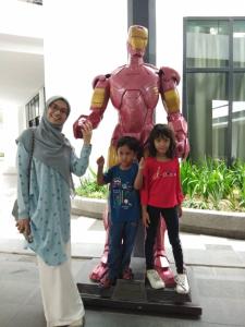 莎阿南Tini Icity Guesthouse的一名妇女和两名儿童站在超级英雄雕像旁边