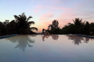 莫尔吉姆StayVista Ashore 6BHK Infinity Pool Ocean View- Morjim的日落时坐在游泳池边的女人