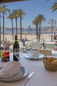 贝尼多姆科隆酒店的一张桌子、一瓶葡萄酒和一张享有海滩美景的桌子