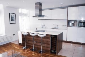 曼彻斯特Deansgate Luxury Apartments的厨房配有白色橱柜和带凳子的台面