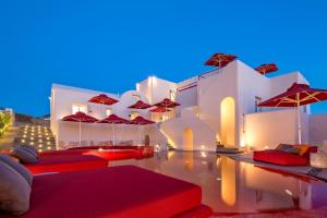 皮尔戈斯圣托里尼艺术酒店的一座游泳池旁,配有红色枕头和遮阳伞