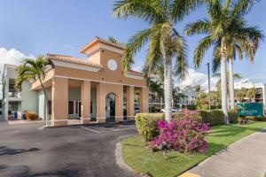 布卡拉顿Quality Inn Boca Raton University Area的停车场内种有棕榈树和鲜花的建筑