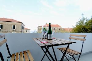 乌马格La Piazza的阳台上配有一张桌子和两把椅子,并提供一瓶葡萄酒