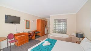 科夫斯港Country 2 Coast Motor Inn Coffs Harbour的一间卧室配有一张床、一张书桌和一个浴缸