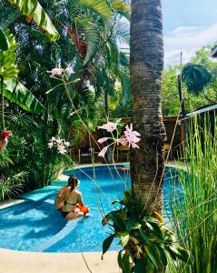 塔马林多Ten North Tamarindo Beach Hotel的坐在棕榈树旁边的游泳池里的女人