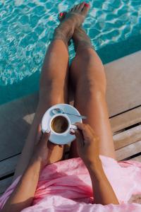 帕图马塞里亚摇篮住宿加早餐旅馆的躺在泳池前的女人,拿着一杯咖啡
