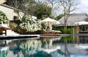 努沙杜瓦REVĪVŌ Wellness Resort Nusa Dua Bali的房屋旁的游泳池配有遮阳伞和椅子