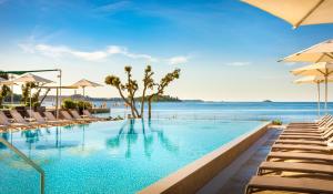 罗维尼Maistra Select Amarin Resort的毗邻大海的带椅子和遮阳伞的游泳池