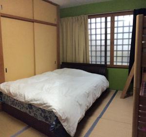 京都上桂旅馆的一间卧室配有一张带白色床单的床和两个窗户。