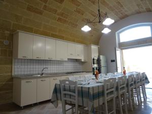 莱乌卡Dimora Rizzo con tappeti di pietra的厨房配有带白色橱柜和椅子的长桌