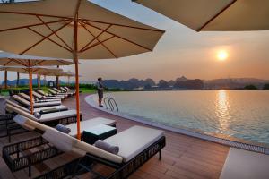 下龙湾FLC Halong Bay Golf Club & Luxury Resort的水边的躺椅和遮阳伞