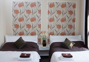 伦敦261酒店的一间卧室设有两张床,墙上贴有橙花。