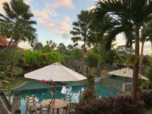 乌布巴厘岛贝图图别墅旅馆的一个带椅子和遮阳伞的游泳池,并种植了棕榈树