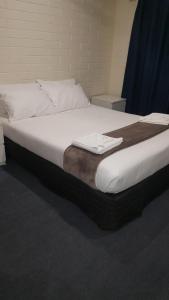 阿德莱德Lockleys Hotel的一张铺有白色床单的床和一张棕色的毯子