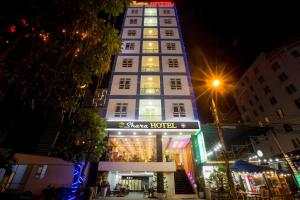 岘港Shara Hotel Da Nang的一座高大的白色建筑,晚上有商店前