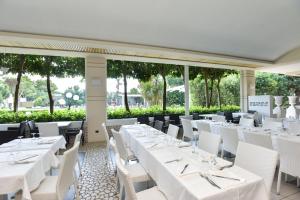 乌真托Hotel Club Astor的餐厅设有白色的桌子和白色的椅子及窗户。