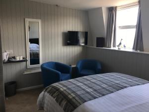 桑德斯富特Woodlands Guest House的一间卧室配有2把蓝色椅子和1张床以及电视。