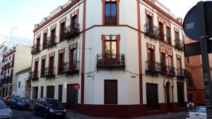 塞维利亚Hub Hostel Seville的带阳台的建筑和停在街上的汽车