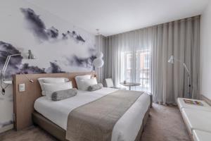 图卢兹格兰德巴康酒店的卧室配有一张大床,墙上挂有绘画作品