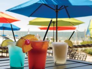 迈尔斯堡海滩钻石顶点海滩度假酒店的桌子上放着一把雨伞,放着三杯饮料