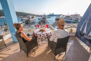 切什梅蛤蜊别墅酒店的两人坐在阳台上的桌子上,船上有船只