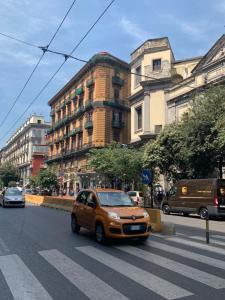 那不勒斯Maison Arena Al Corso的一辆橙色汽车沿着城市街道行驶,街道上有许多建筑