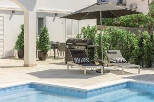特罗吉尔Villa Gala的一个带两把椅子和一把遮阳伞的庭院,毗邻一个游泳池