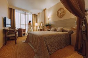 喀山Olymp Kazan的一间酒店房间,房间里有一张床,一个女人站在窗户旁