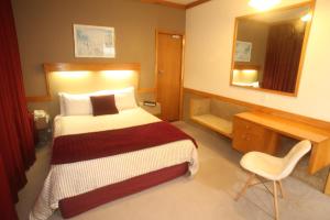 旺格努伊The Grand Hotel Wanganui的一间卧室配有一张床、一张书桌和一面镜子