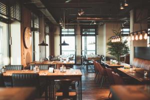 威廉港Fliegerdeich Hotel & Restaurant的餐厅设有木桌、椅子和窗户。