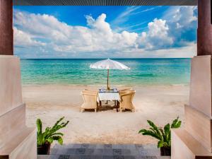 查汶Montien House - SHA Plus的海滩上的一张桌子,上面摆放着遮阳伞和椅子
