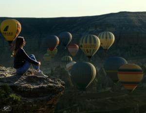格雷梅Kayatas Cave Suites的坐在悬崖上的女人看着一束热气球