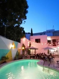 坎昆Moloch Hostel & Suites的夜间游泳池,配有桌子和遮阳伞