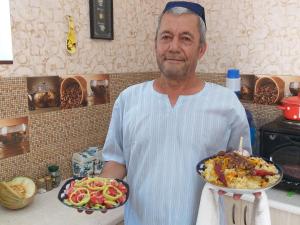 布哈拉Zafar Family Guesthouse的站在厨房里拿着两盘食物的人