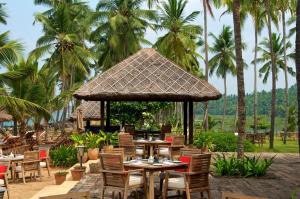 可瓦兰Taj Green Cove Resort and Spa Kovalam的一间设有桌椅的餐厅,种植了棕榈树