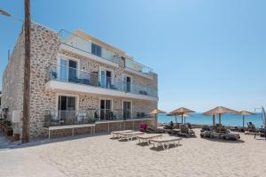 卡尔扎迈纳Kyma Rooms & Suites的海滩上的一座建筑,配有桌子和遮阳伞
