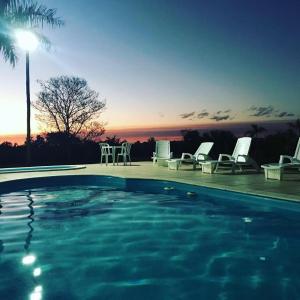 沙帕达-杜斯吉马朗伊斯Pousada e Restaurante Valle dos Ventos的一个带椅子的游泳池,享有日落美景