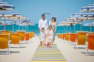 朱利亚诺瓦帕克德普林西比酒店的家庭在海滩上散步,并带椅子和遮阳伞