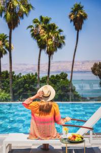 提比里亚基内瑞特湖畔别墅酒店的坐在长凳上的女人看着游泳池