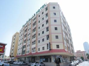 阿吉曼Al Rayan Hotel的一座高大的粉红色建筑,汽车停在停车场